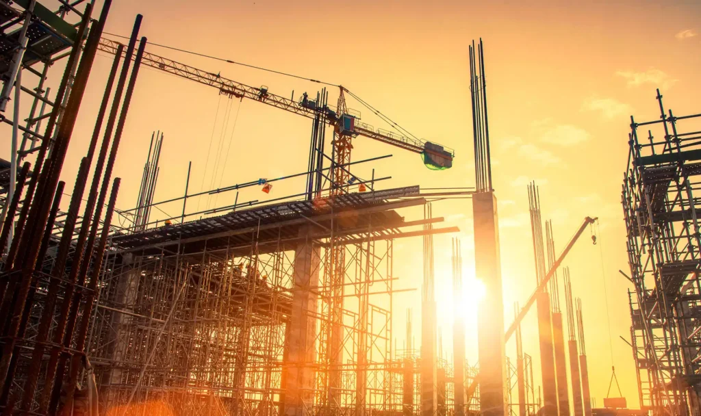 Construction site at sunset with cranes, scaffolding, and workers building reinforced concrete structures, representing Icon Group’s contractor and construction services.